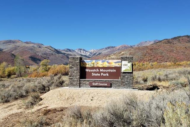 Wasatch Mountain State Park sign with autumn-colored mountains and hills in the background