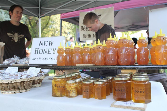 A variety of honey bottles on a table in a farmers market stand