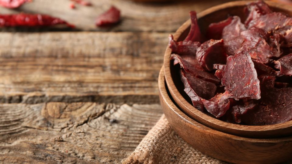 A wooden table with a wood bowl with beef jerkey