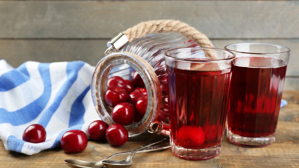 Cherries coming out of a bottle onto a table an red cherry drinks sitting near