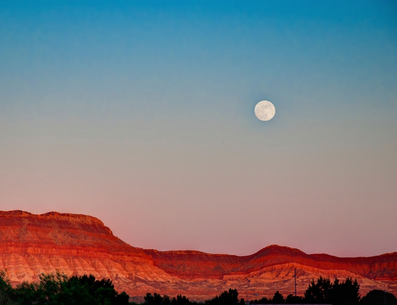 the moon in the sky with red rocks in the background