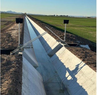 Concrete irrigation canal running through an agricultural field, with water flowing along the canal and control structures along the sides.
