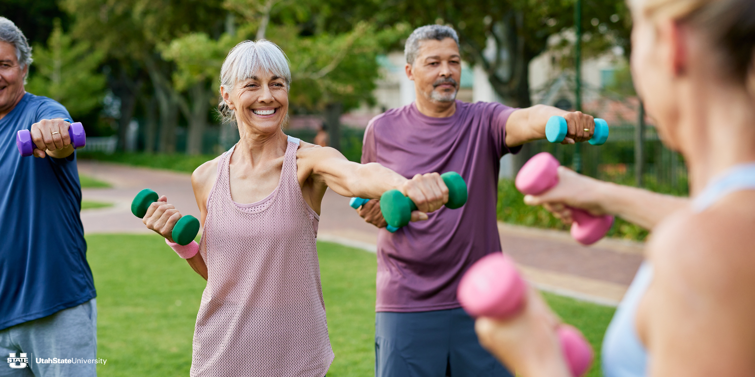 Group of older adults outdoors doing arm exercises with colorful hand weights in a park setting, smiling and engaged. USU logo in the bottom corner.