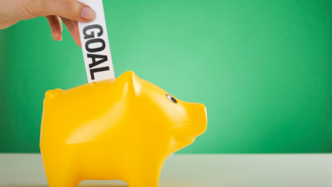 a slip of paper labeled 'goals' being put into a piggy bank