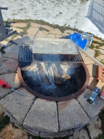 A wide, flat pan sits on a grate above a fire pit.