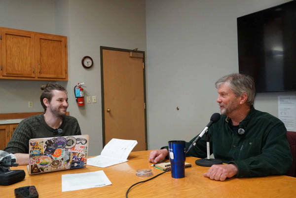 Drew Holley and Darren McAvoy laugh together while sitting at a table with interview equipment