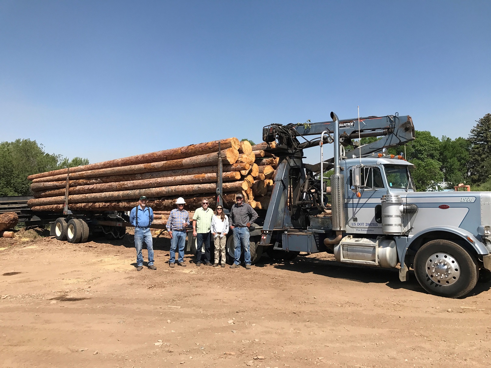 Group of people posing in front of semi truck loaded with lumber