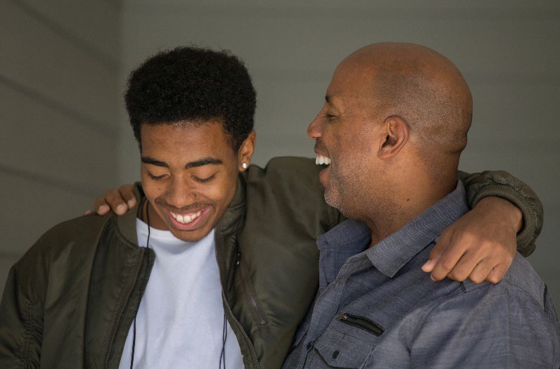 A father with his arm around a teenage boy.