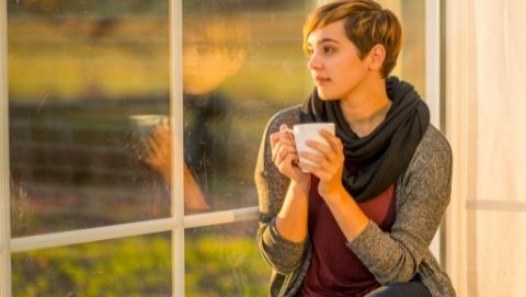 Woman holding coffee looking out window