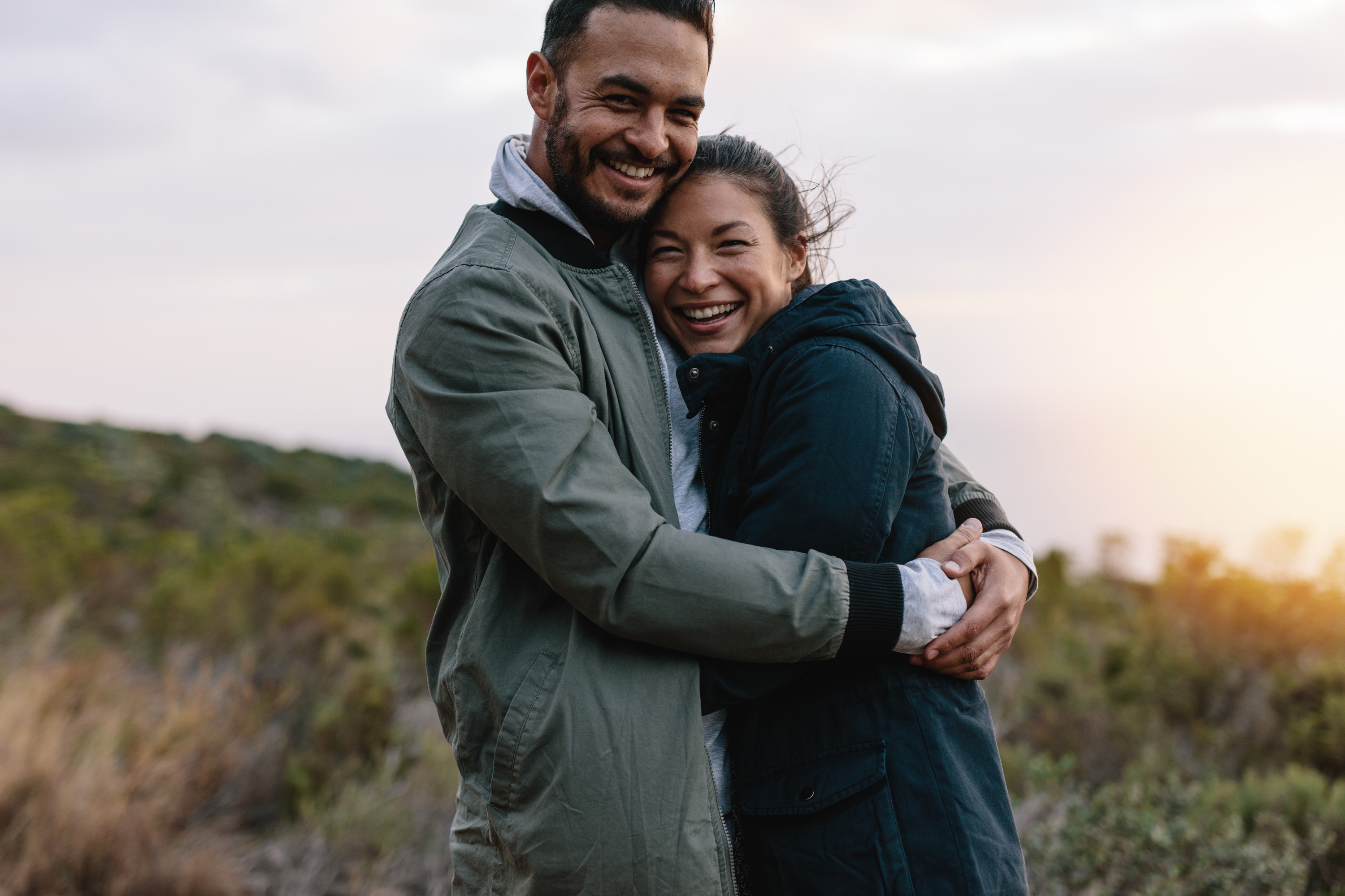 couple hugging each other during sunset while looking into the camera