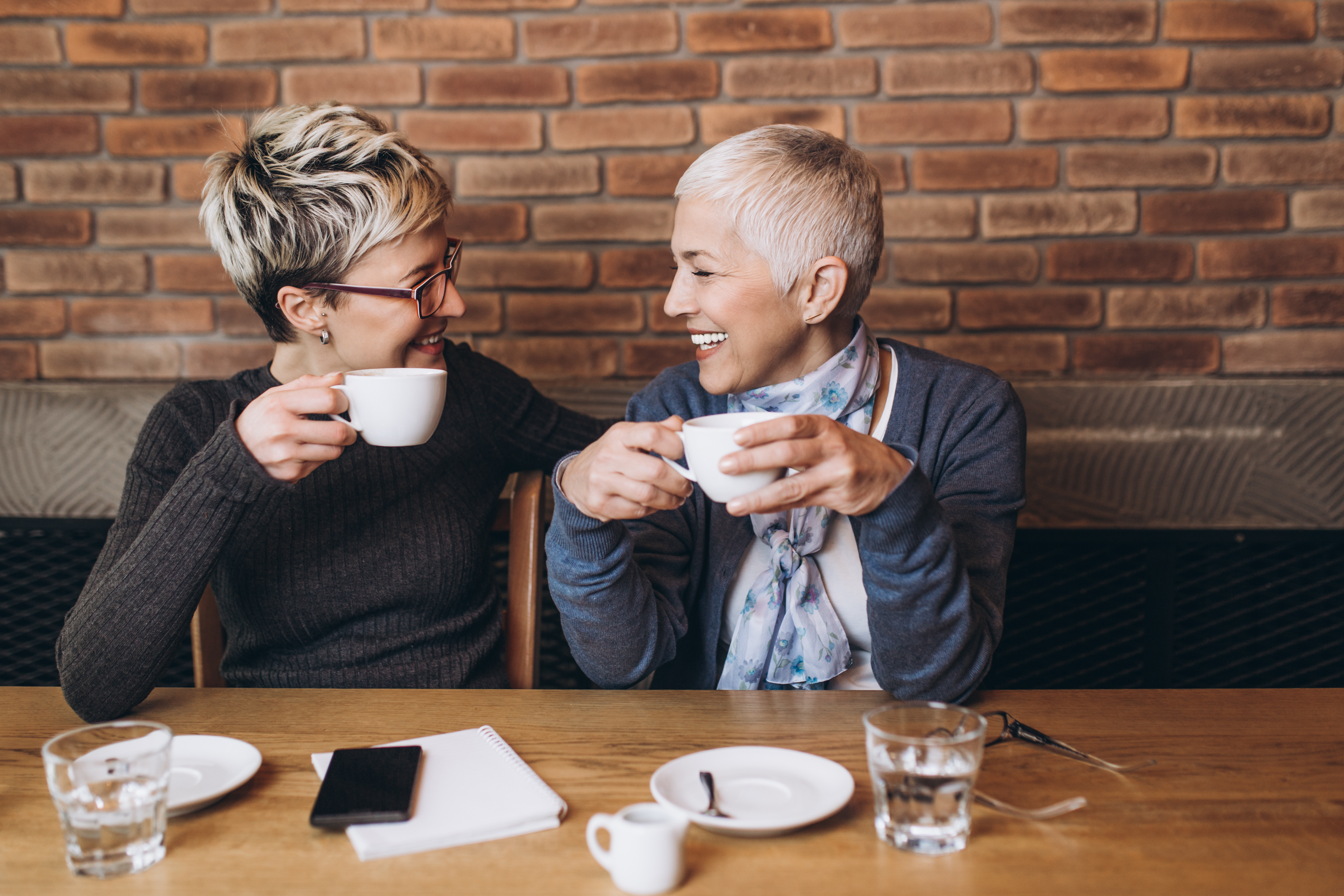 female couple laughing together while having coffee at a cozy coffee shop