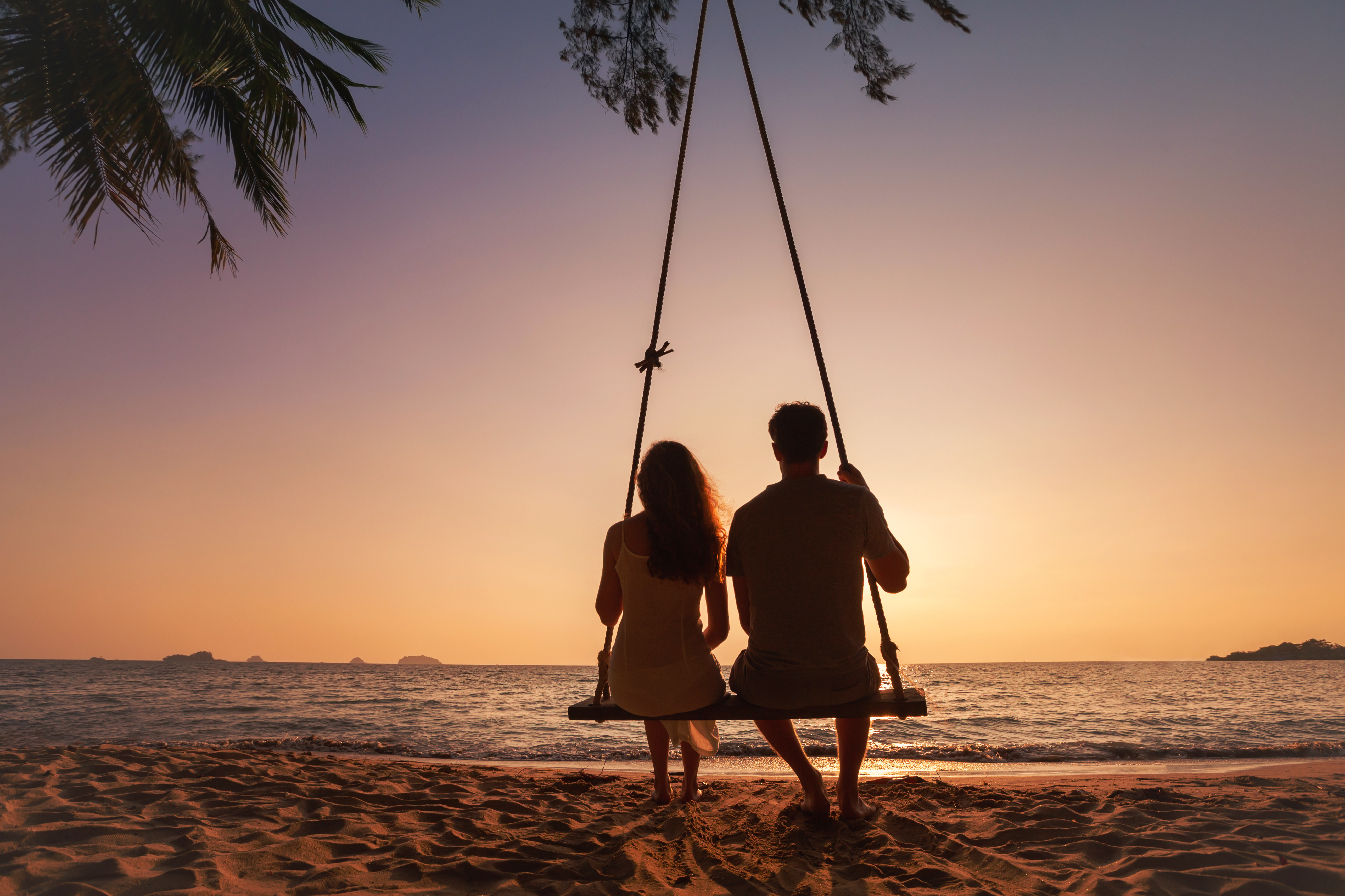 couple sitting on a tree swing during sunset on a beach in front of the ocean