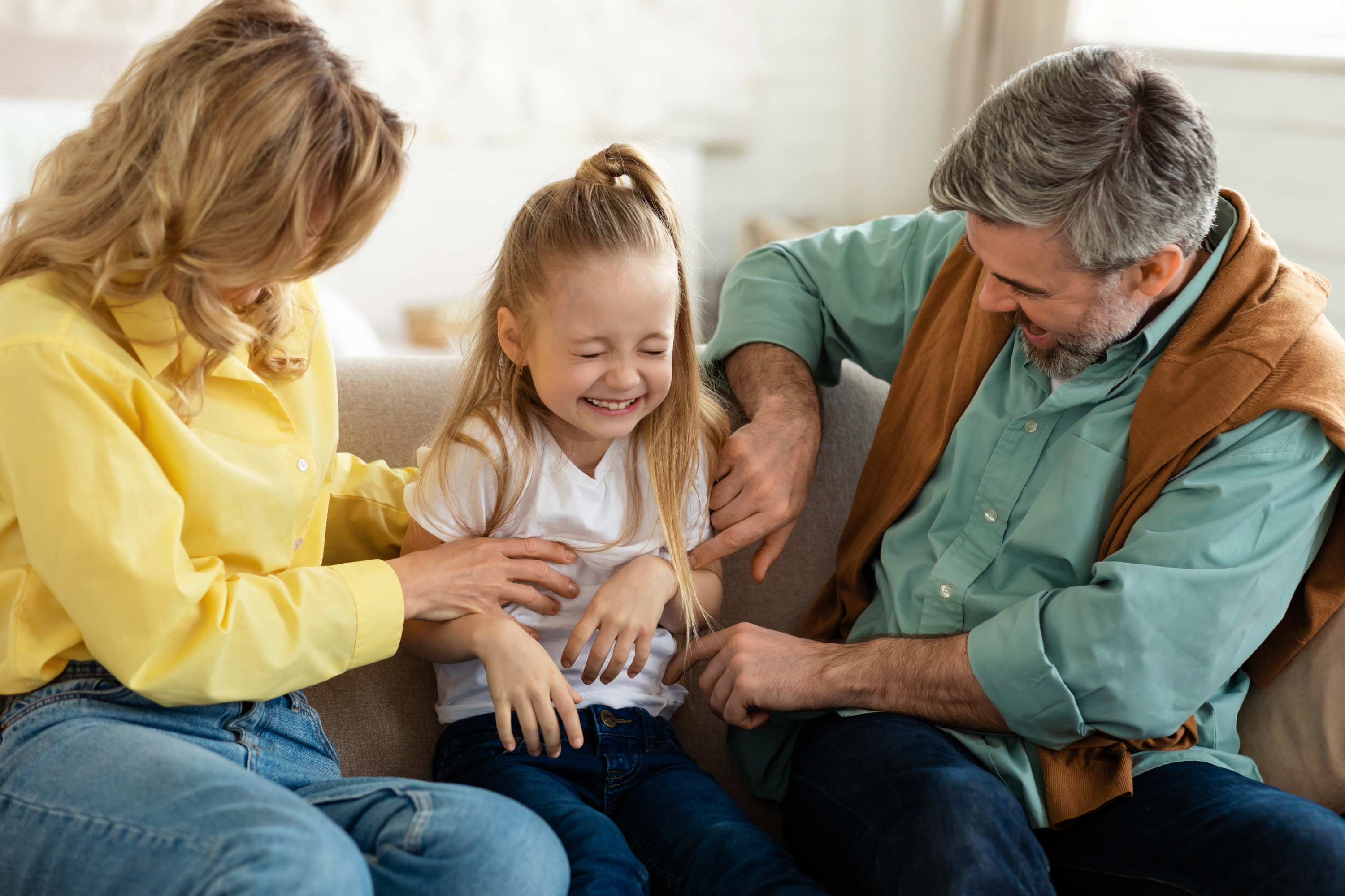 couple tickling their child on a couch