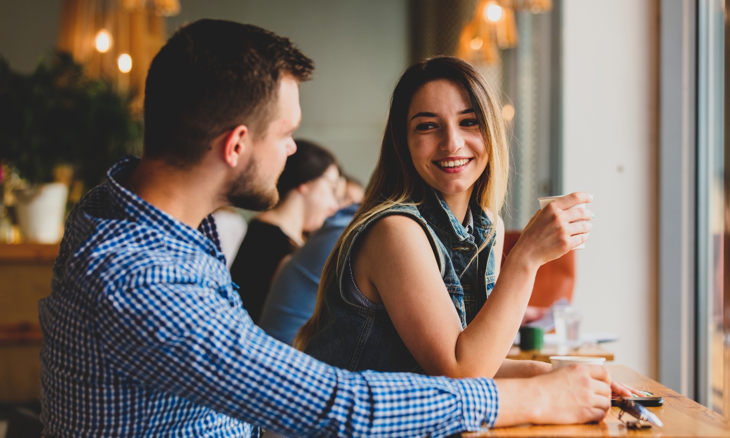 woman smiling at man while sitting together at a bar in a coffee shop