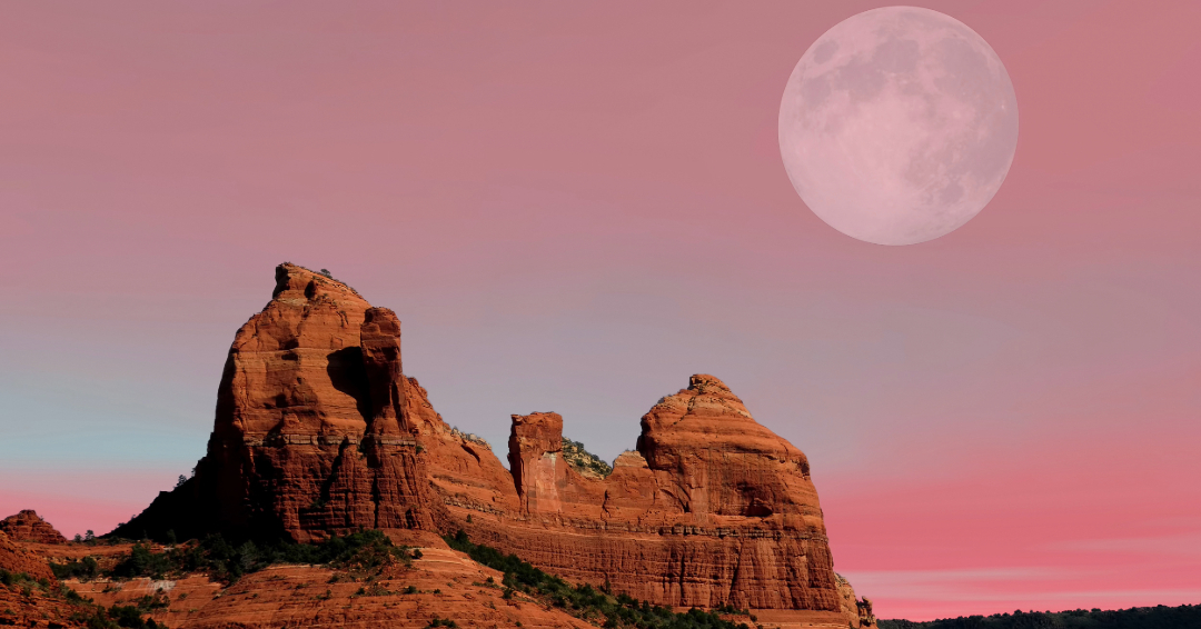 light shining on a butte in Sedona, Arizona with a full moon at sunset