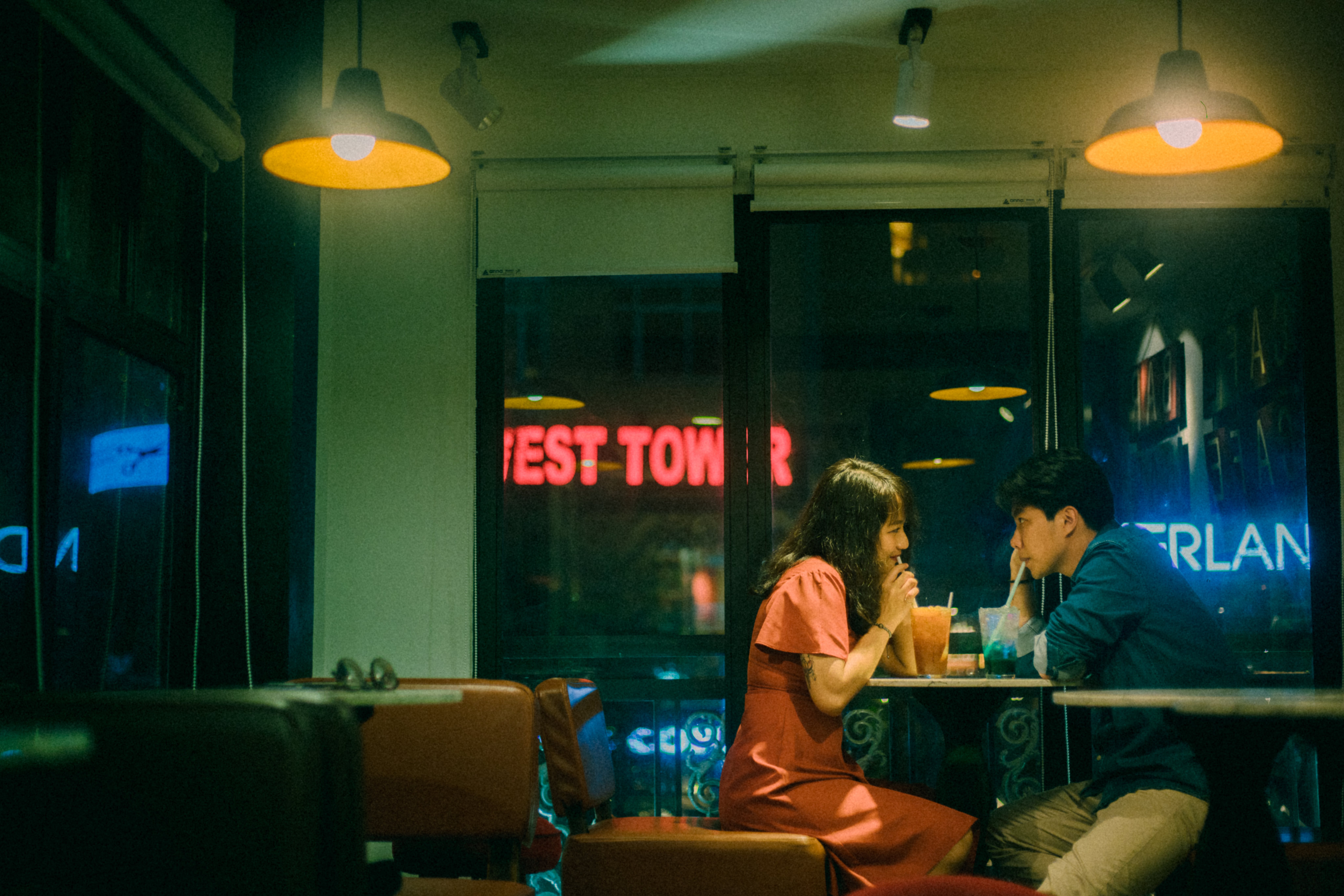 a couple sitting at a table wioth neon signs on glass windows