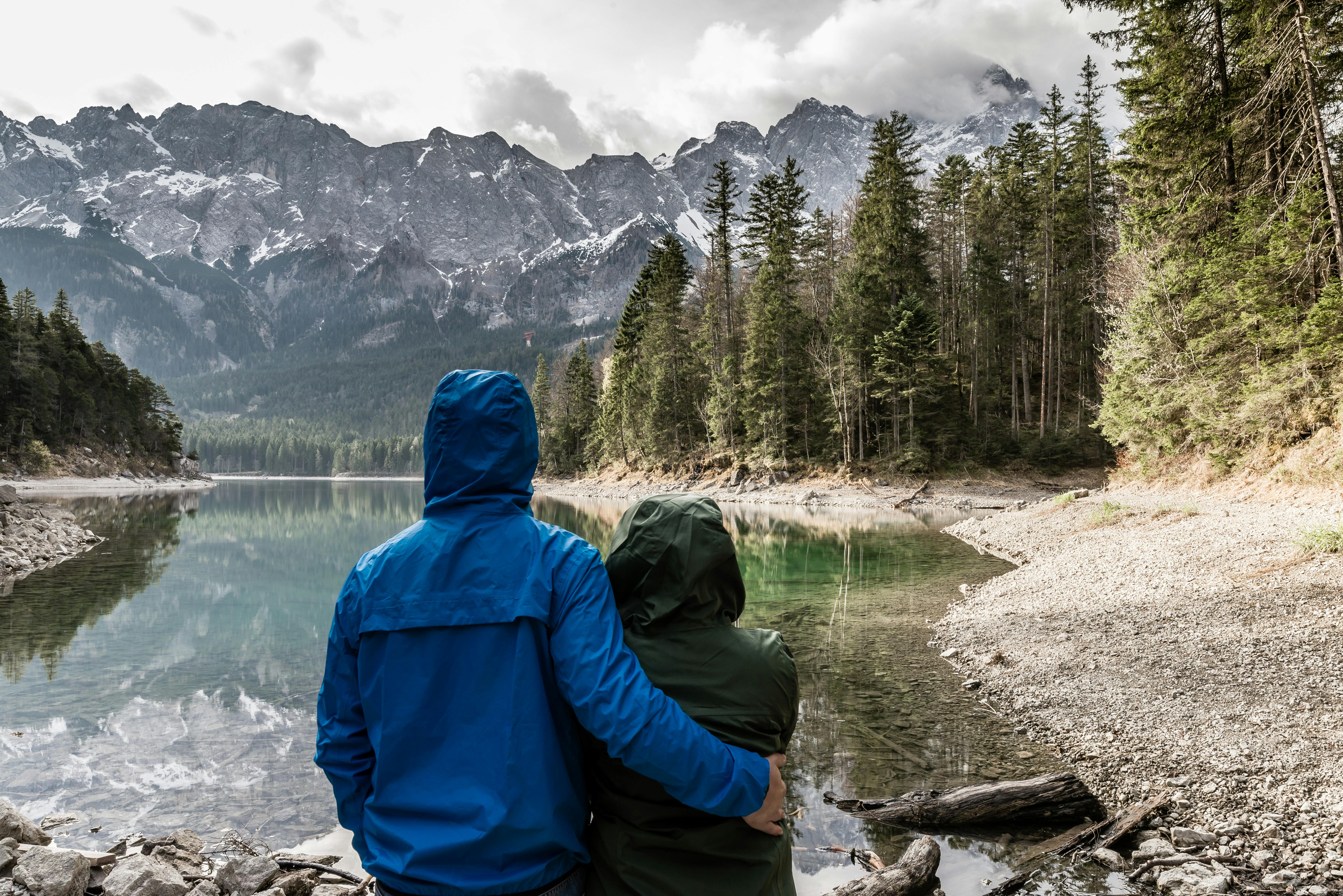couple in raincoats holding each other in front of lake and mountains