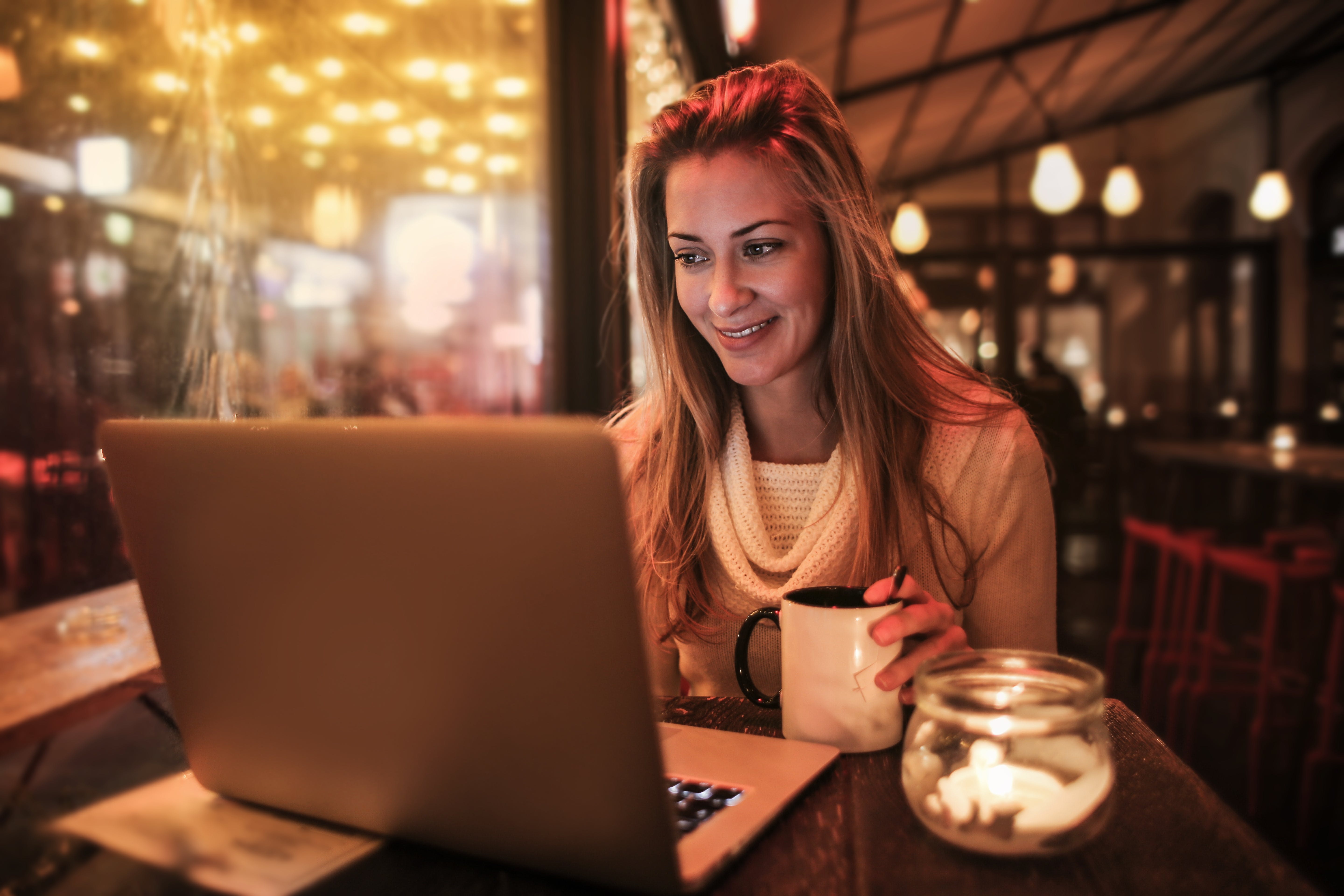 woman smiling while sitting at a table with a laptop and coffee