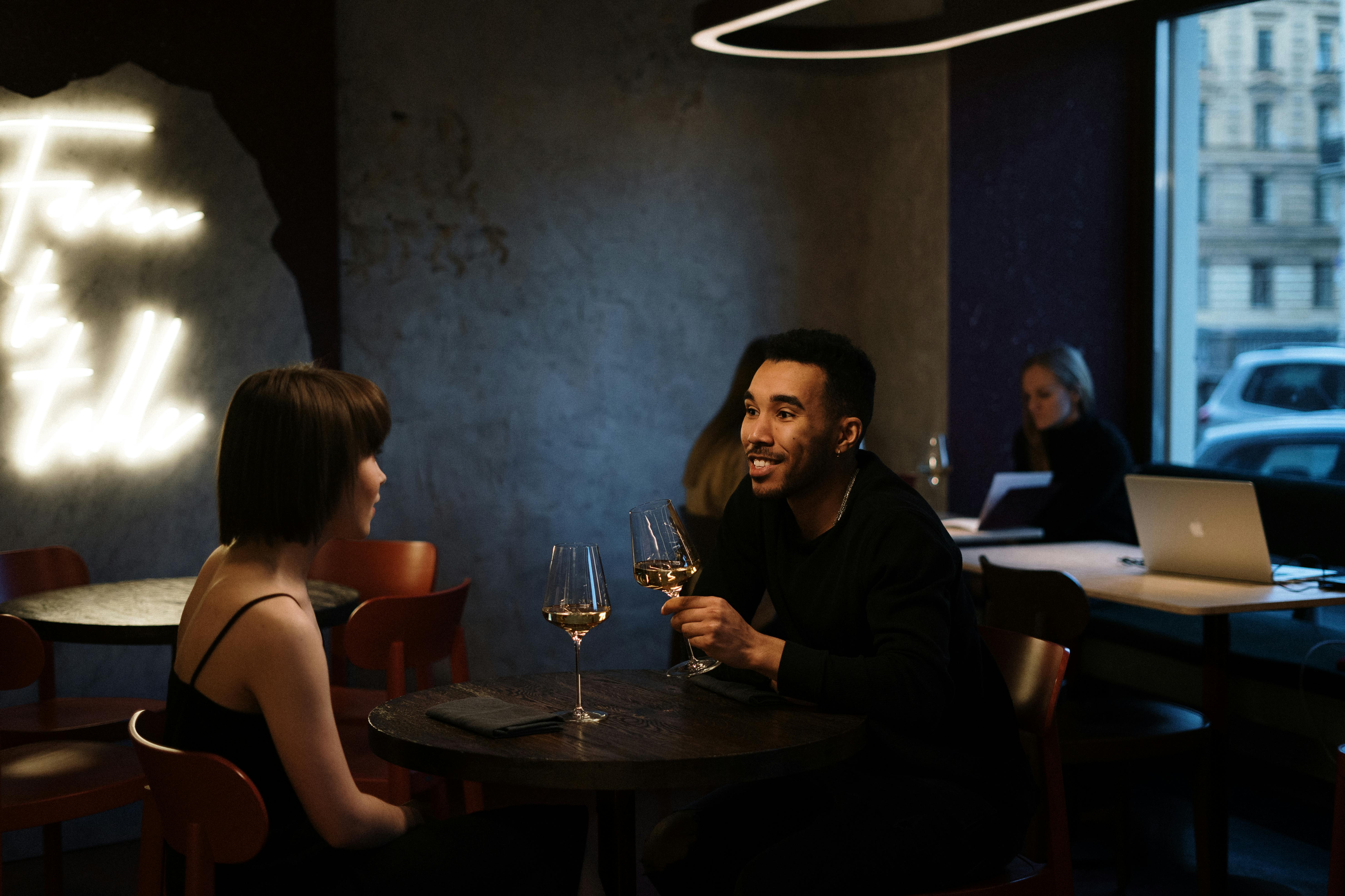 man and woman sitting in a dimly lit restaurant sharing glasses of wine together