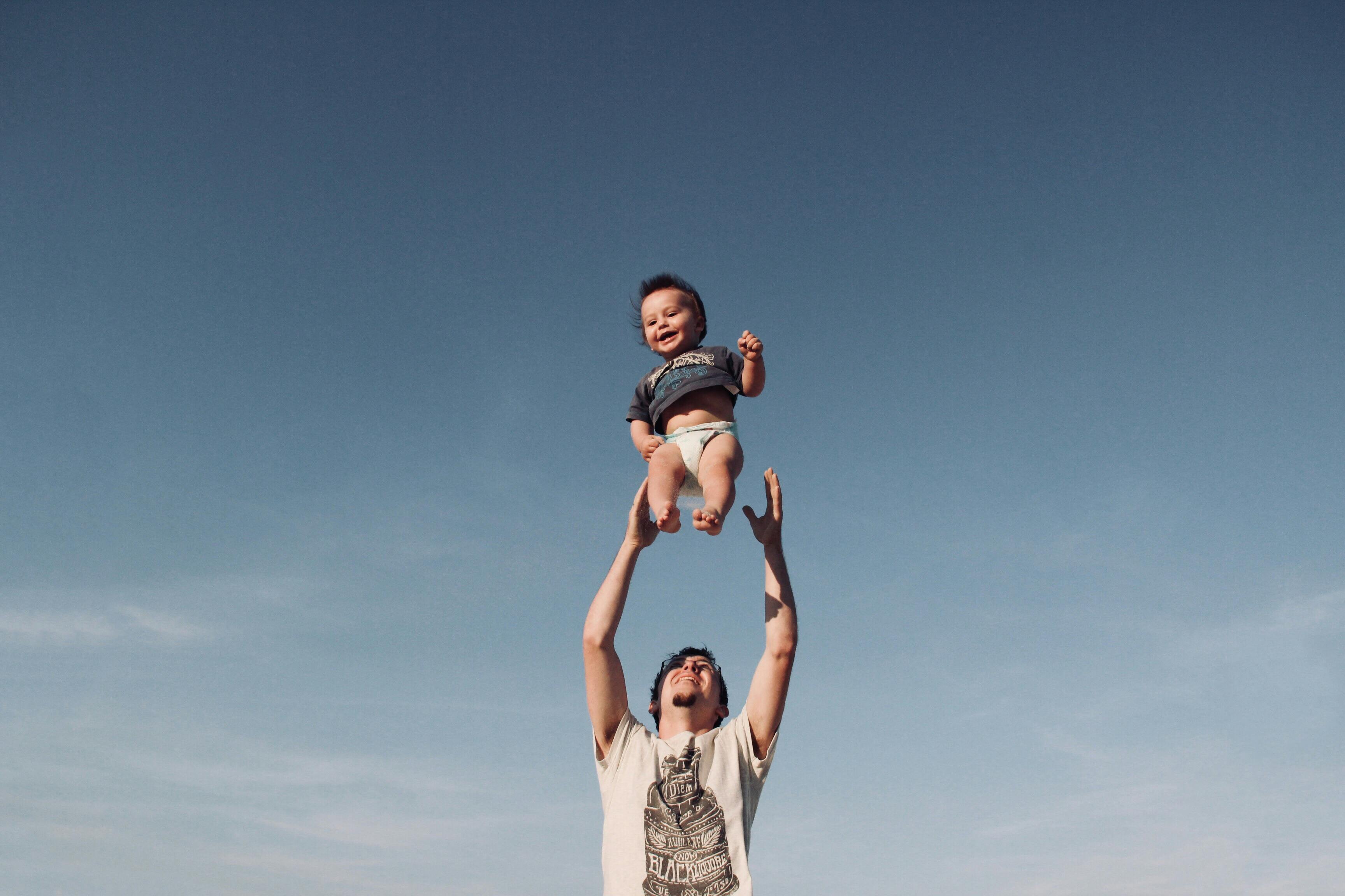 father tossing smiling baby up into the blue sky