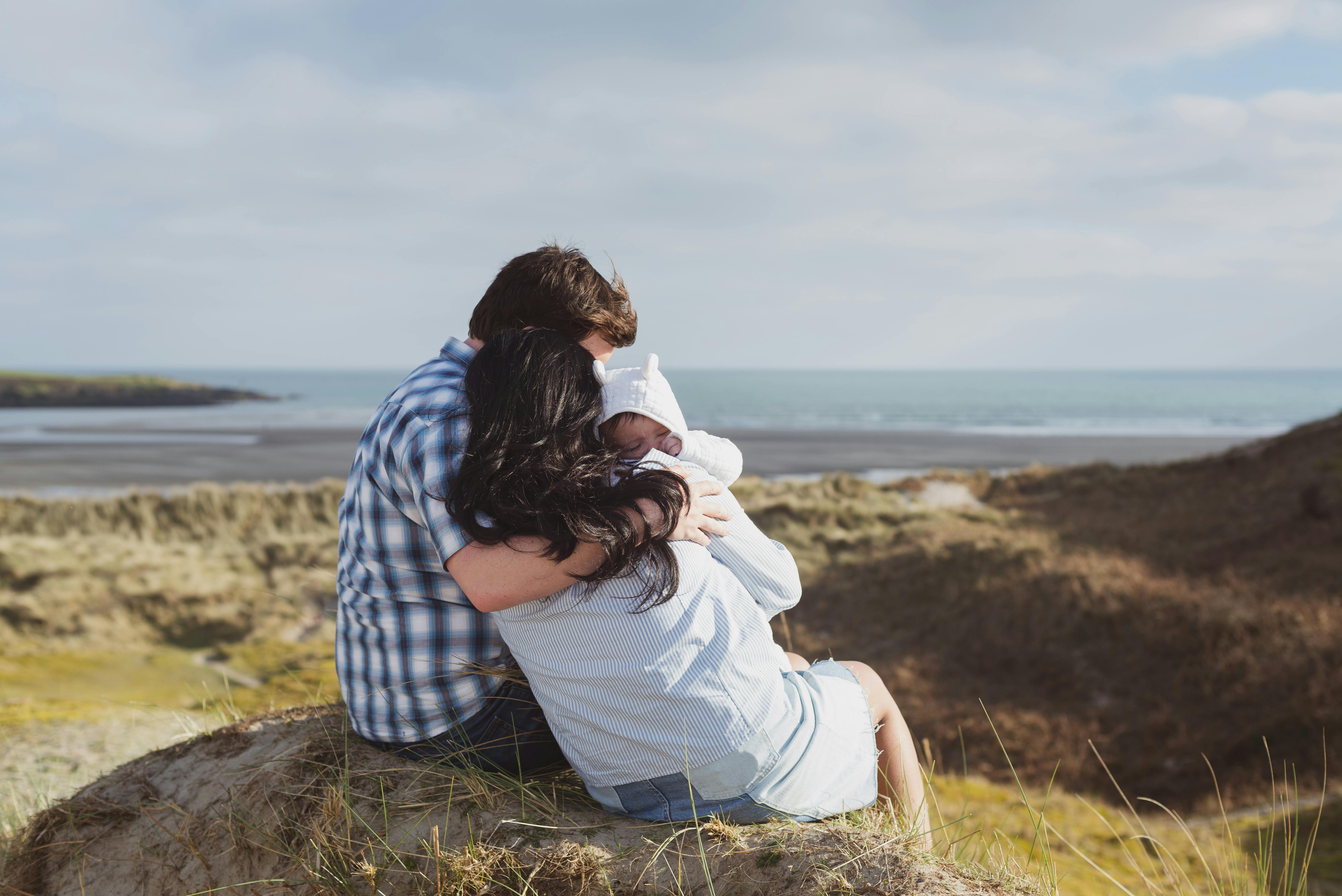 family hugging each other in front of the ocean on a rock