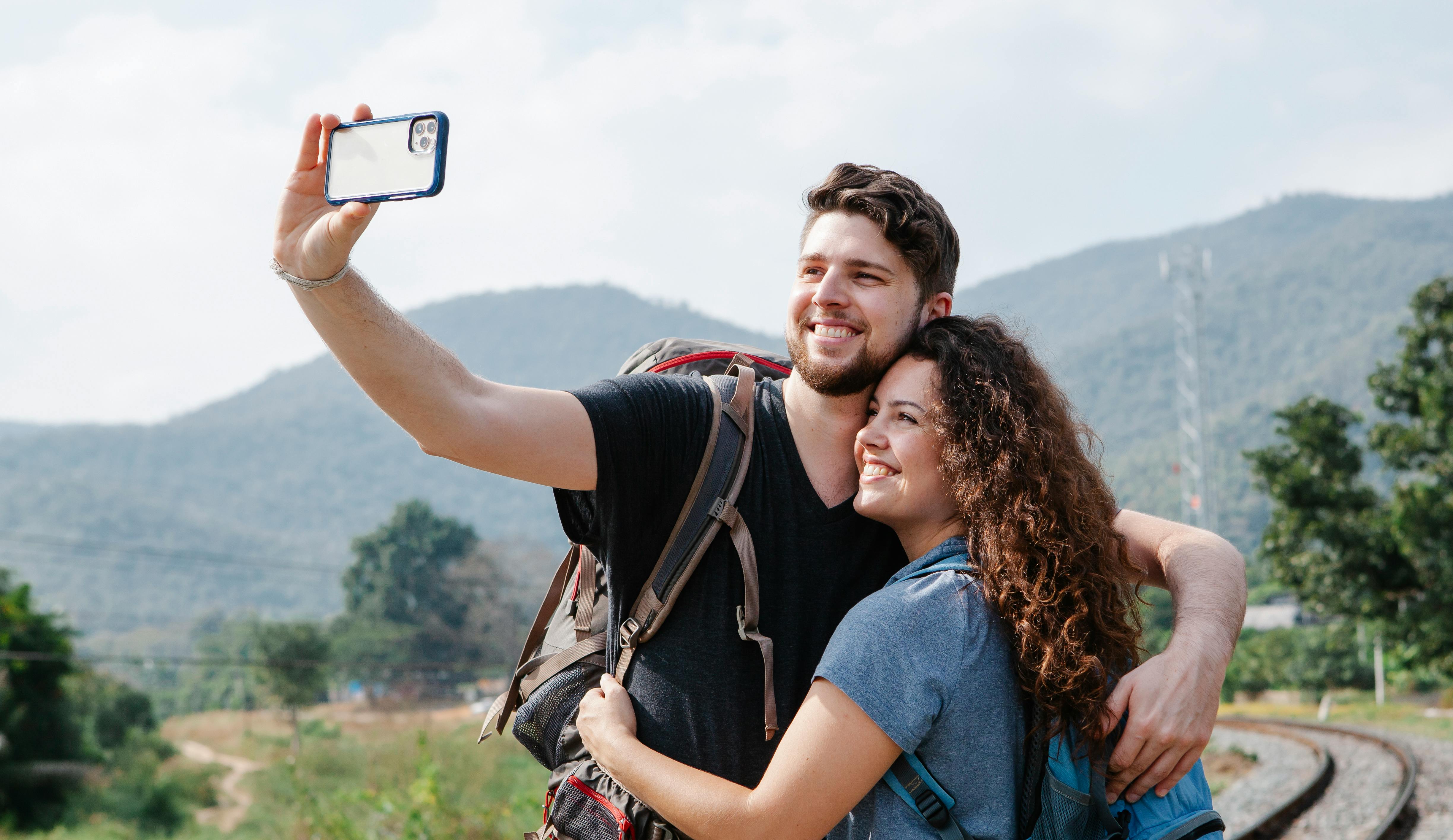 man and woman hugging outside by railroad track while taking selfie