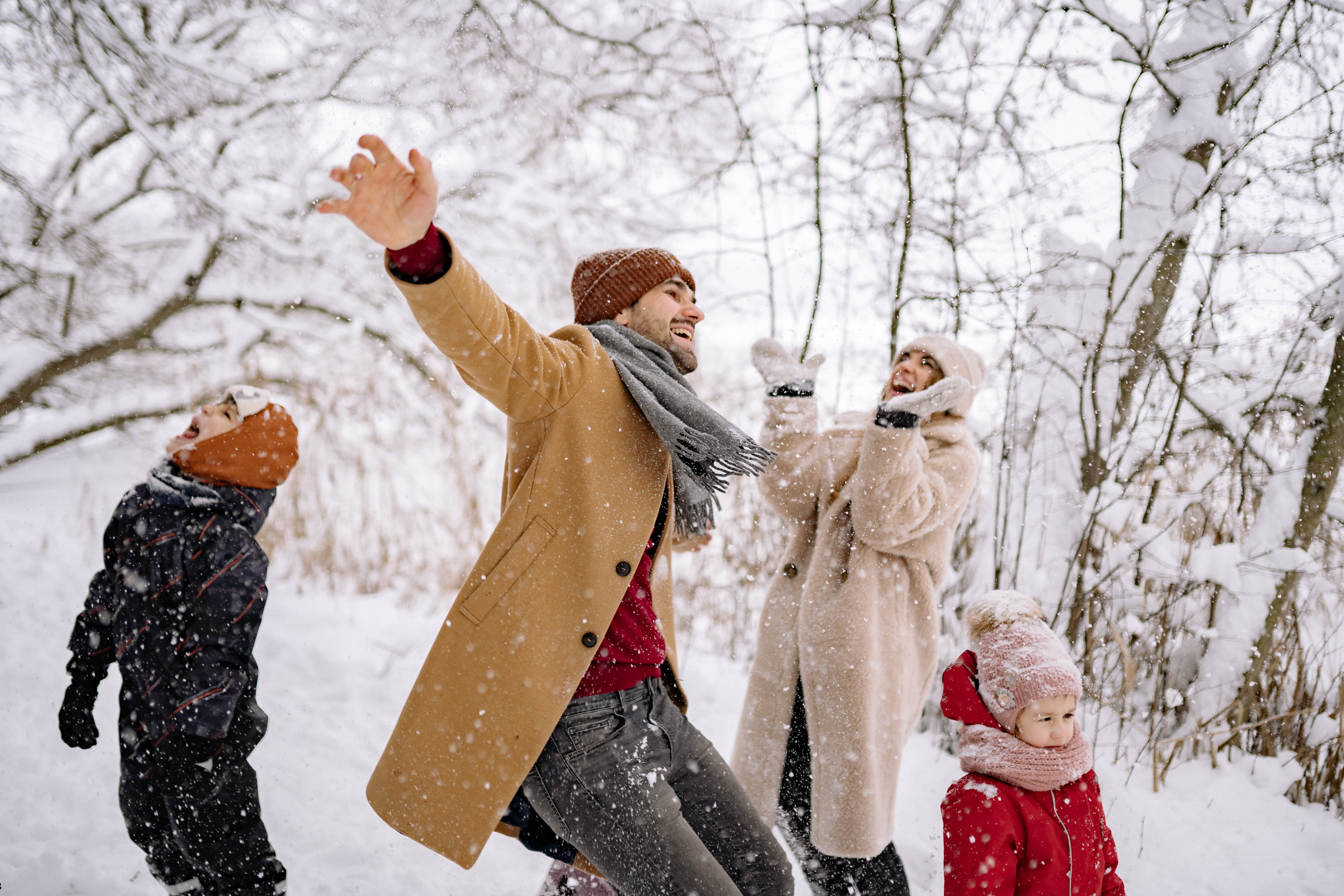 family dancing in falling snow in the woods