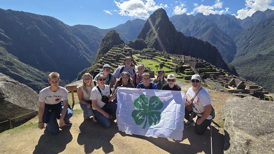 Utah 4-H group poses in front of Machu Pichu, holding a 4-H flag.