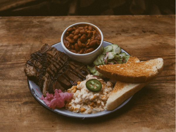 Brisket, corn, beans, pickled onions and cucumbers, with two slides of toast severed on a plate