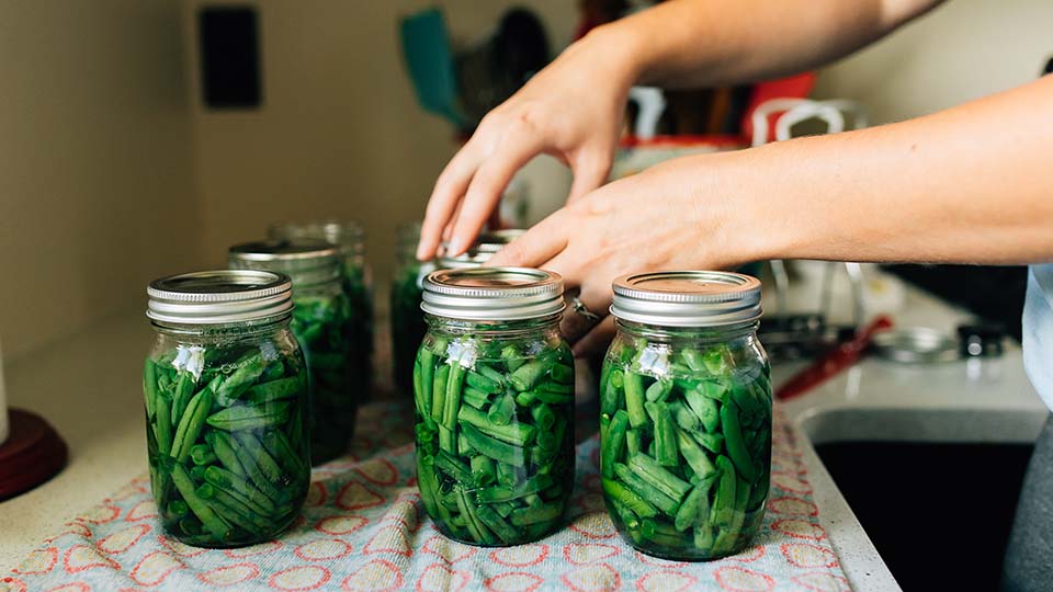 A woman securing screw bands on mason jars filled with green beans during home canning.