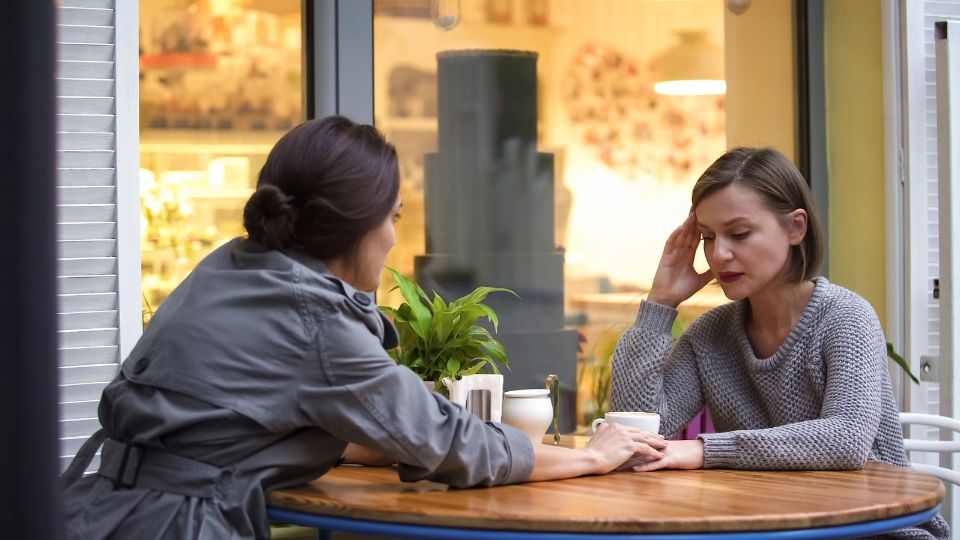 A women comforting another women across a table.