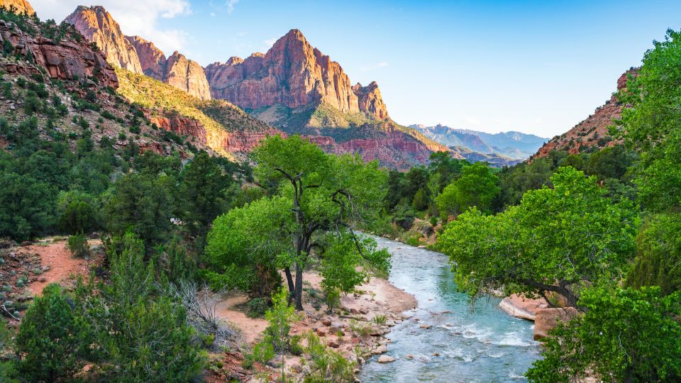 A landscape with a ricer, red rock mountains, and greenery.