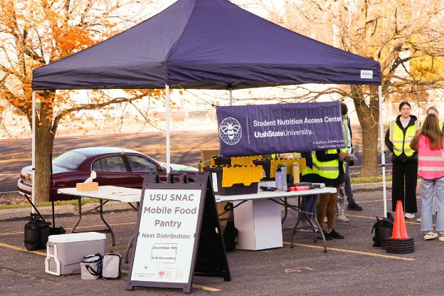 Tent in a parking lot with tables and banners saying things such as USU SNAC Mobile Food Pantry