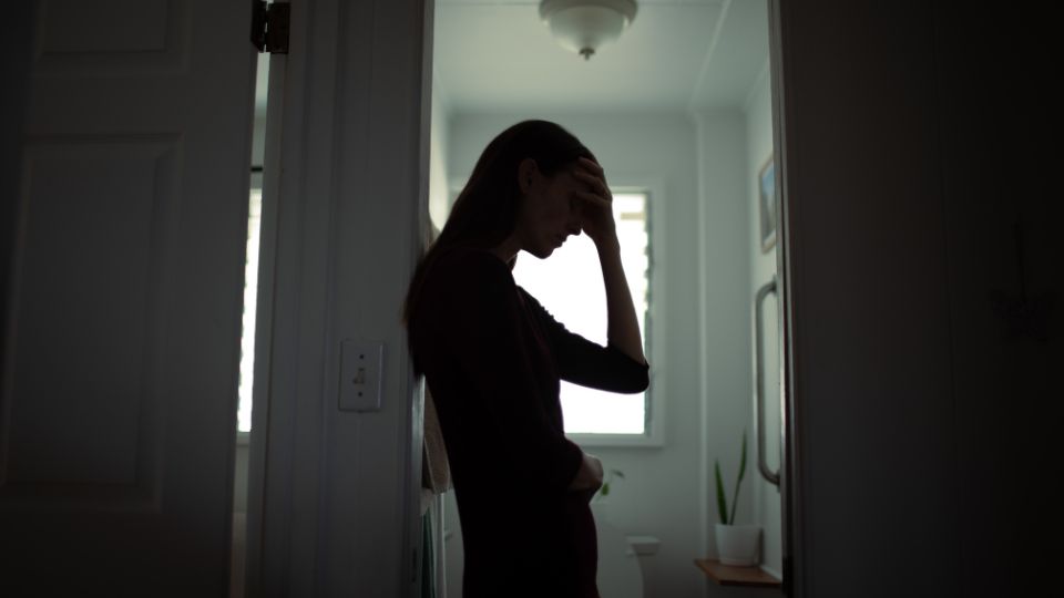 A women standing in a bathroom doorway with a hand on her forehead.