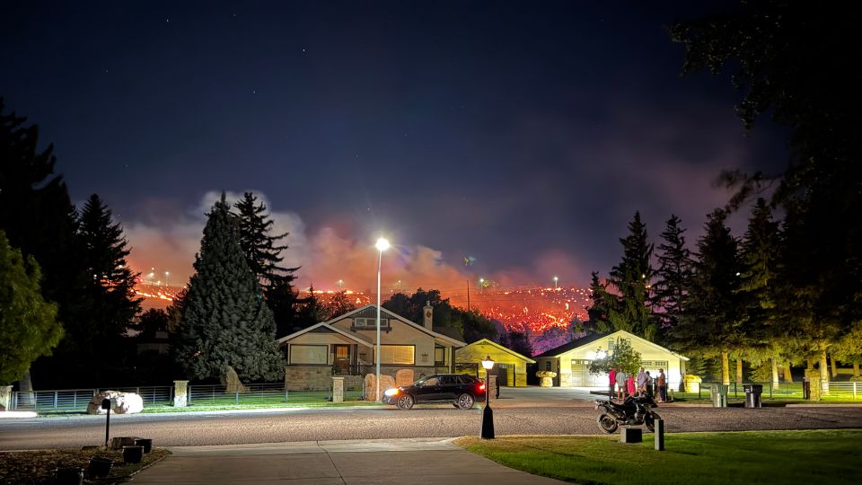 A home with a fire on the hillside behind it.