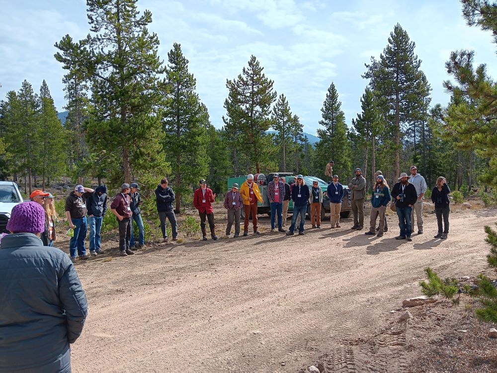 A group of people stand in a semi circle on a dirt road.