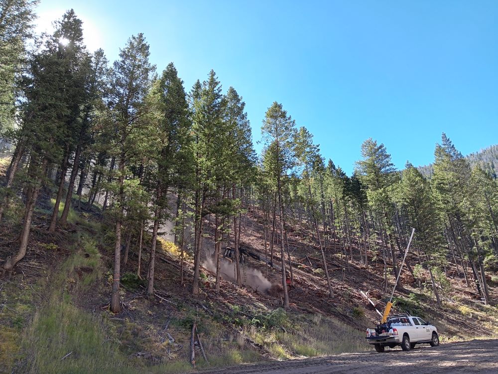 Logging equipment kicks up dust as it slowly descends a steep slope.
