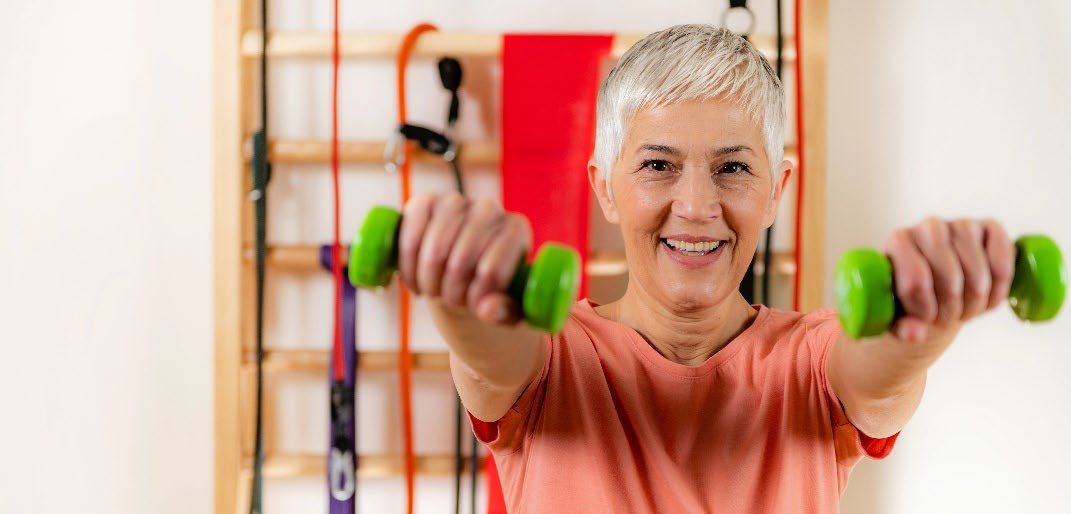 An older women holding small weights infront of her.