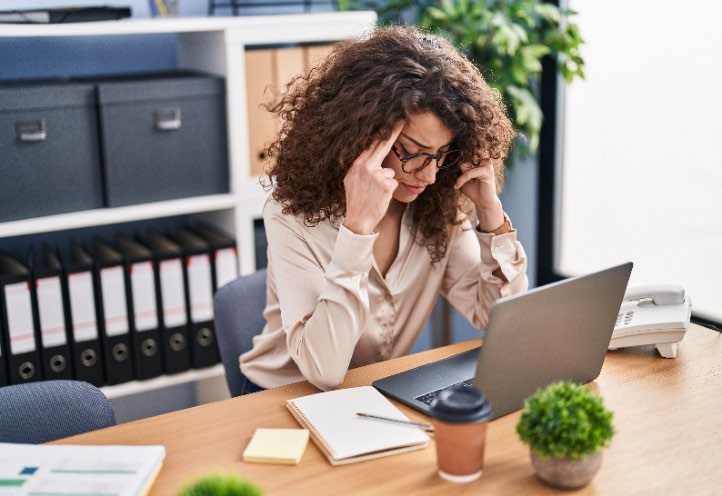 Woman sitting at a desk looking stressed while working on a laptop.