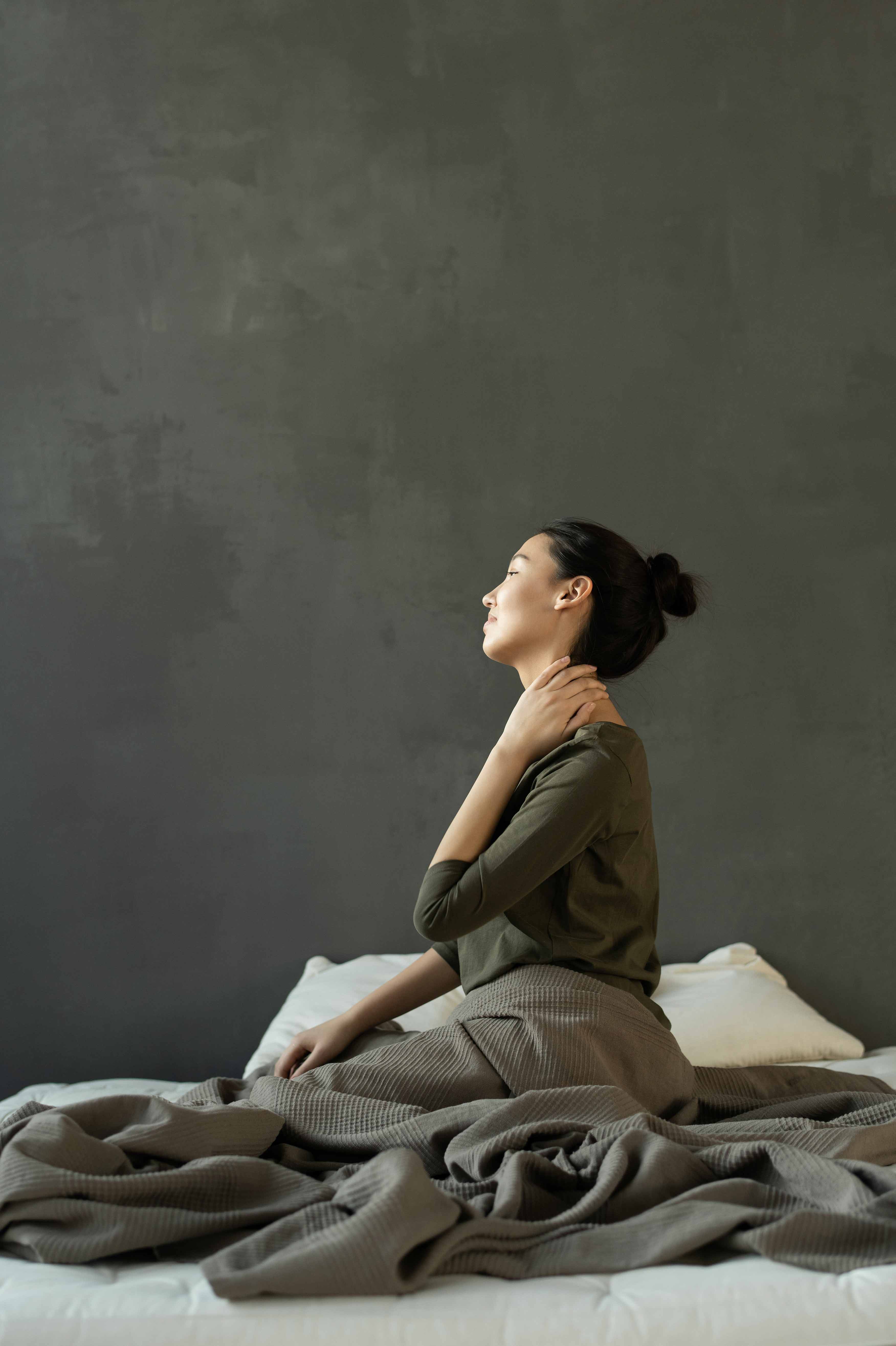 woman kneeling in bed holding her neck