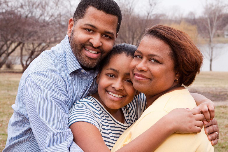 A mother and father hugging their daughter.