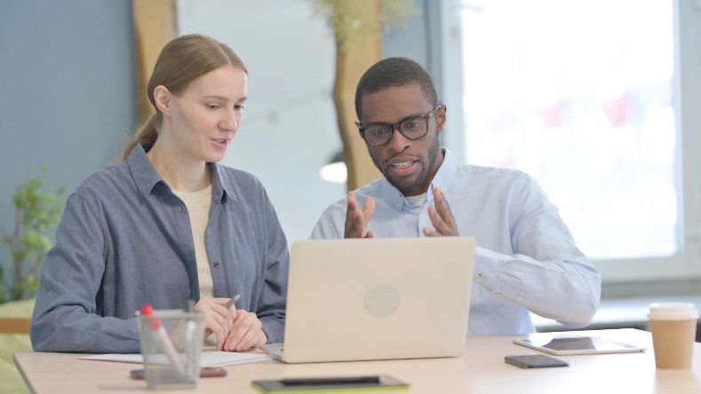 A man and a women having a discussion as they look at a laptop.