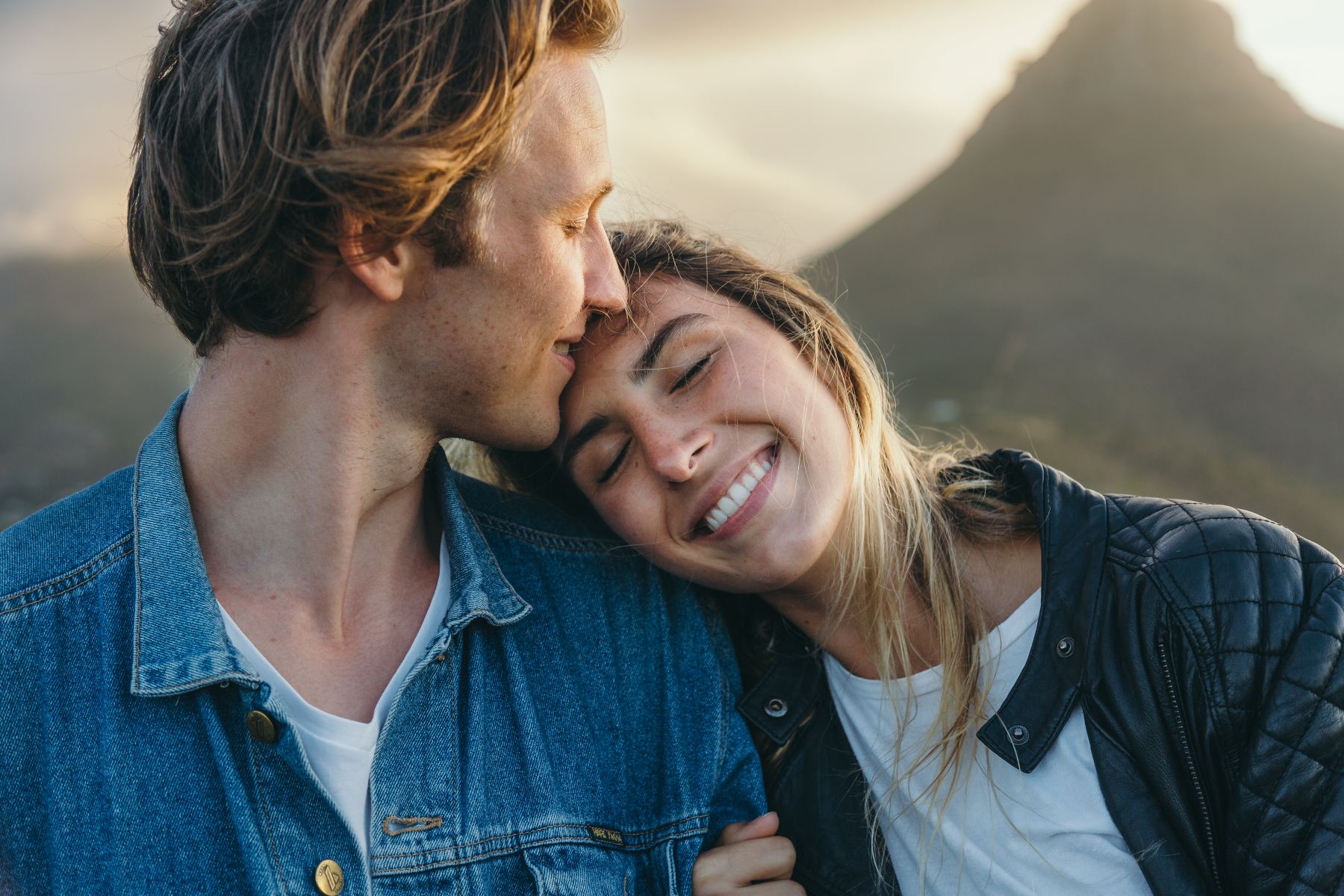 Woman lovingly resting her head on man's shoulder while smiling.