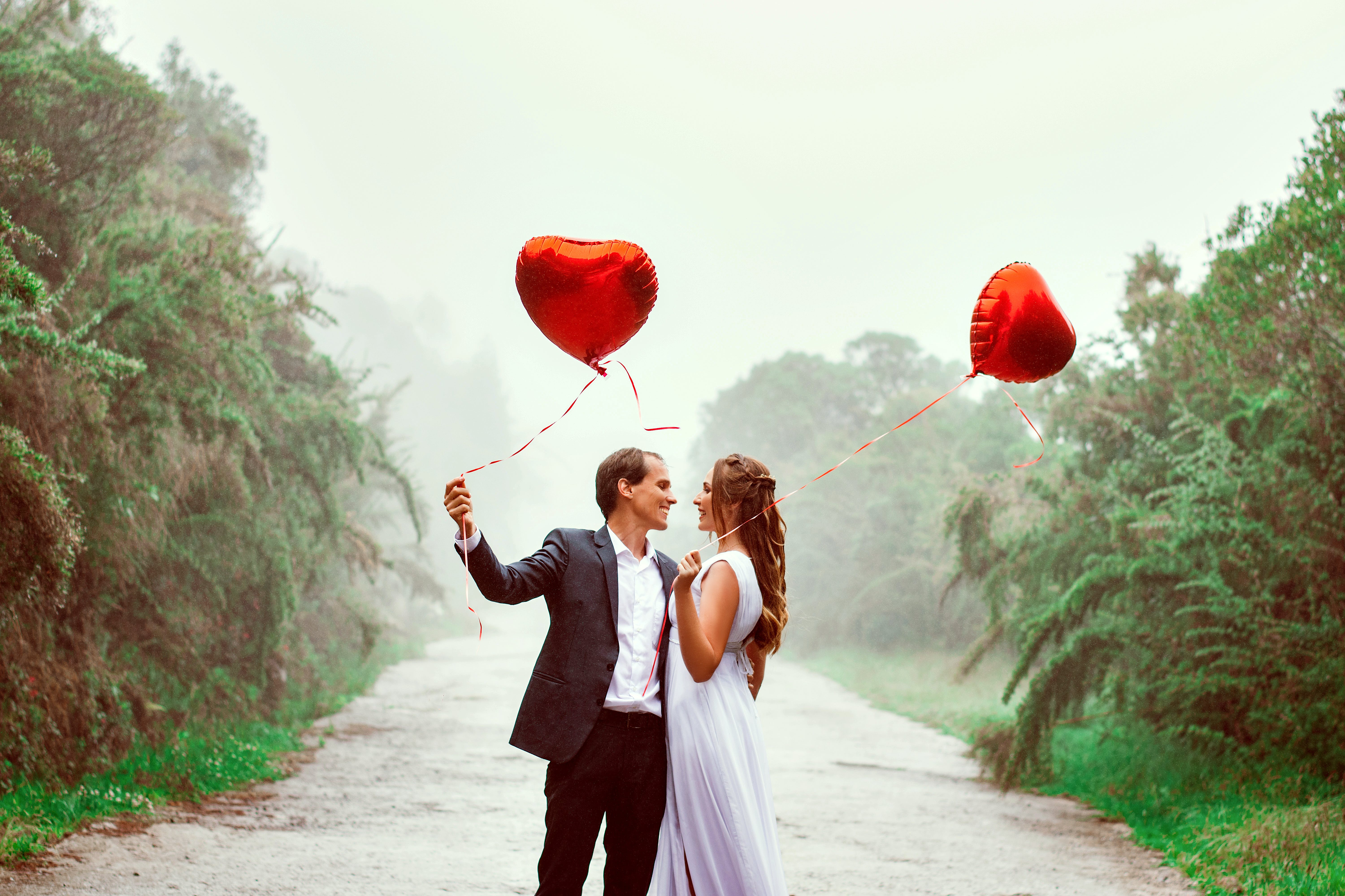 man and woman holding hands while holding red heart-shaped balloons