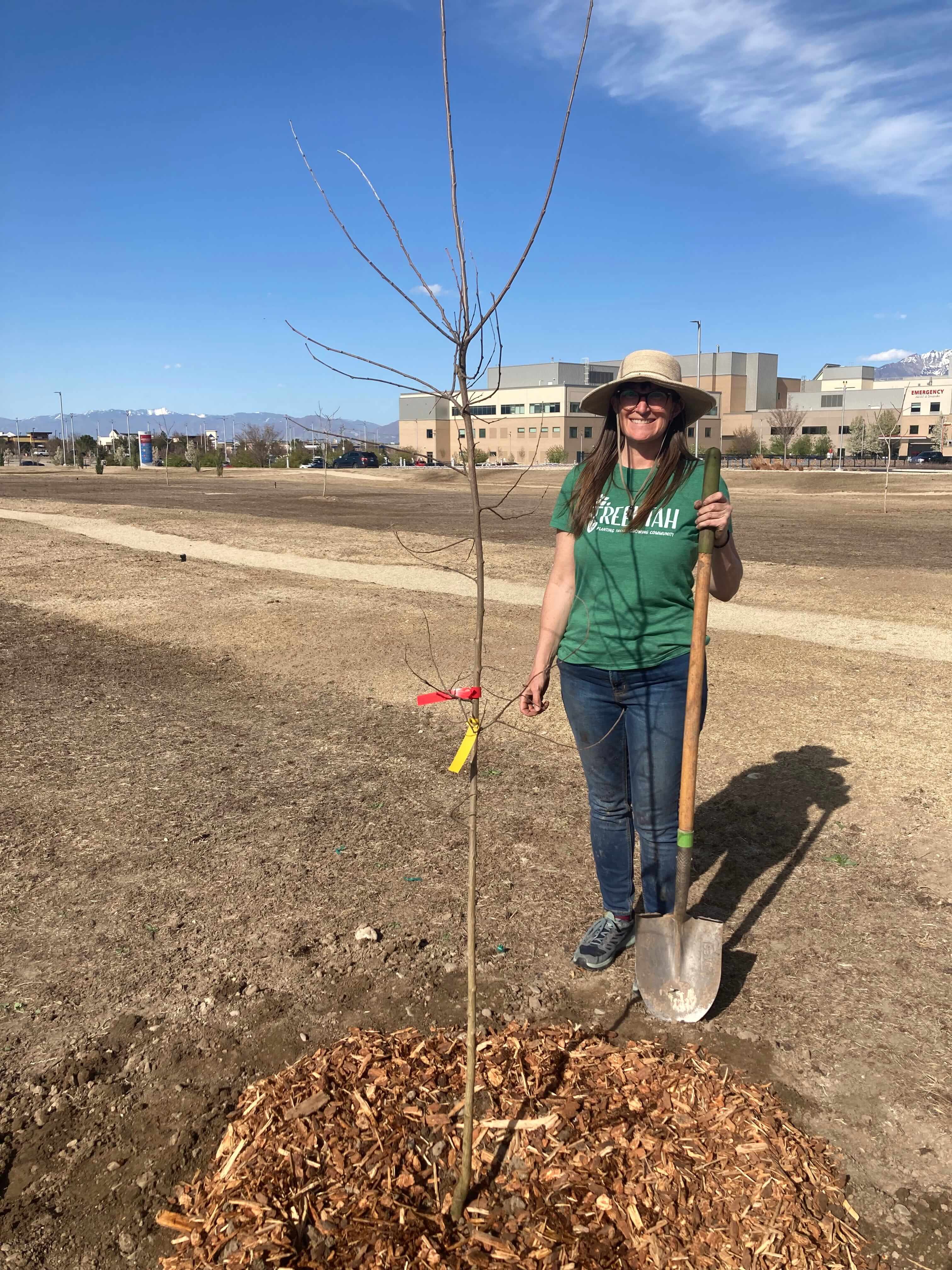 A women witha shovel in front of a freshly planted tree