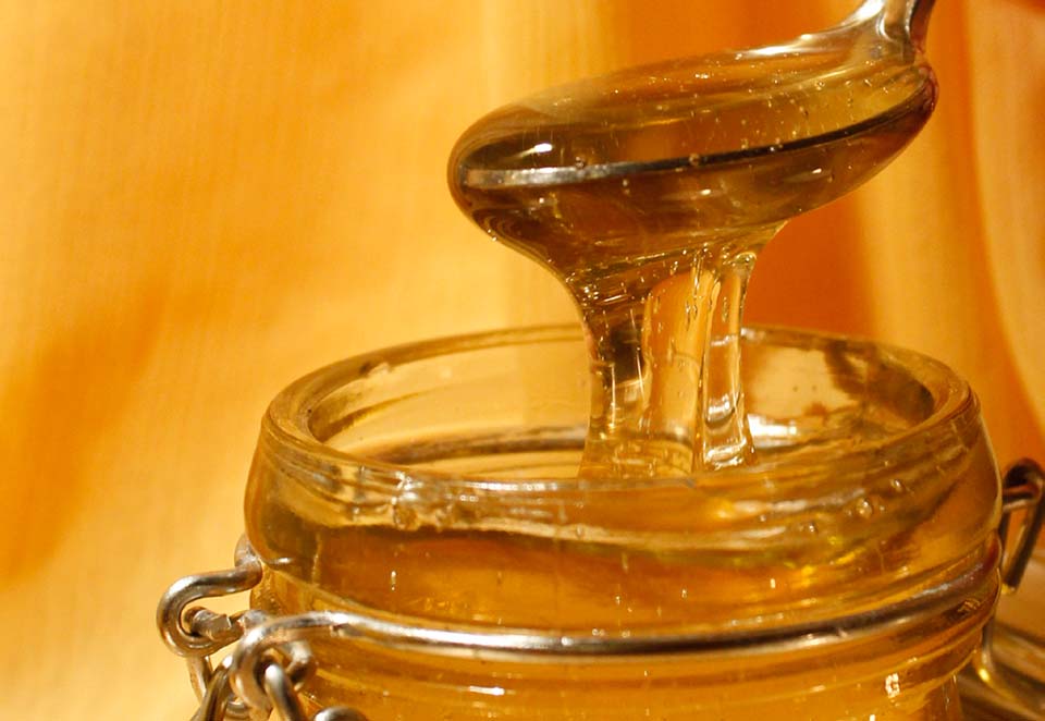 Spoon full of honey being pulled out of glass jar
