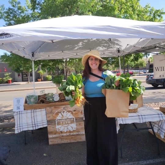 A women holding produce standing at a farmers market stand