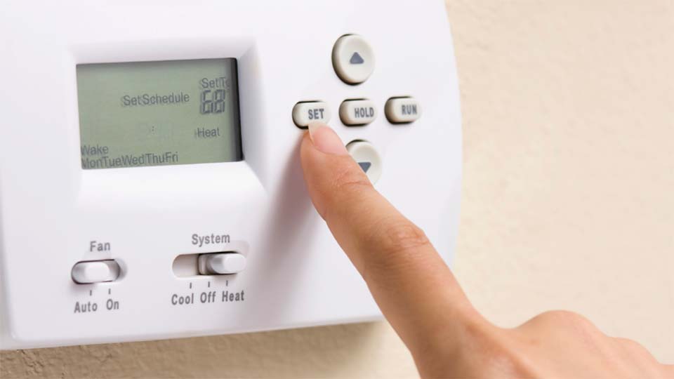 Closeup of finger pressing button to program a thermostat