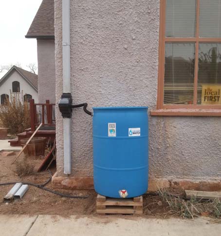 A blue rain barrel at the side of a southewestern style house with xeriscaping