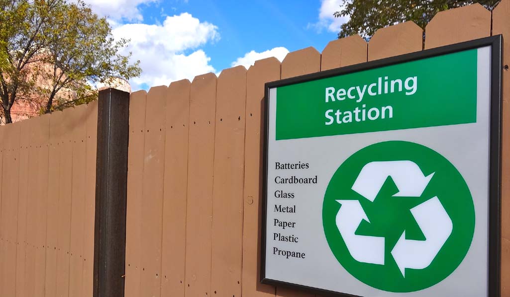 Bold green rycycling sign posted on a picket fence with national park scenary in background